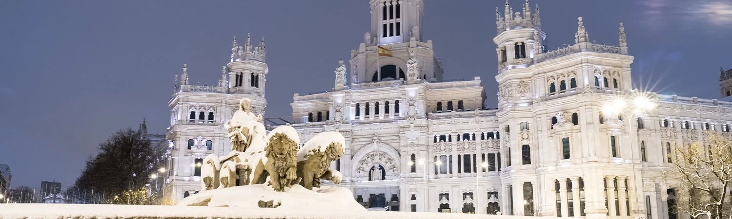 Madrid’s historic and majestic Cibeles Palace with snow and lights under a dark sky.