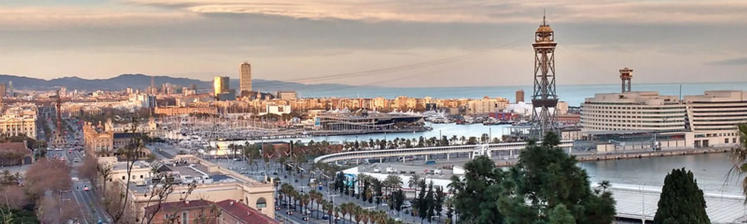 Panoramic view of Barcelona skyline featuring the iconic cable car tower, marina filled with yachts, and modern city architecture at sunset.