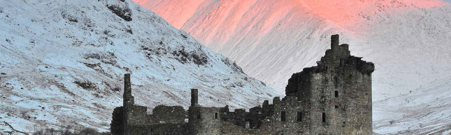The image captures a breathtaking scene of a ruined castle set against the backdrop of snow-covered mountains. 