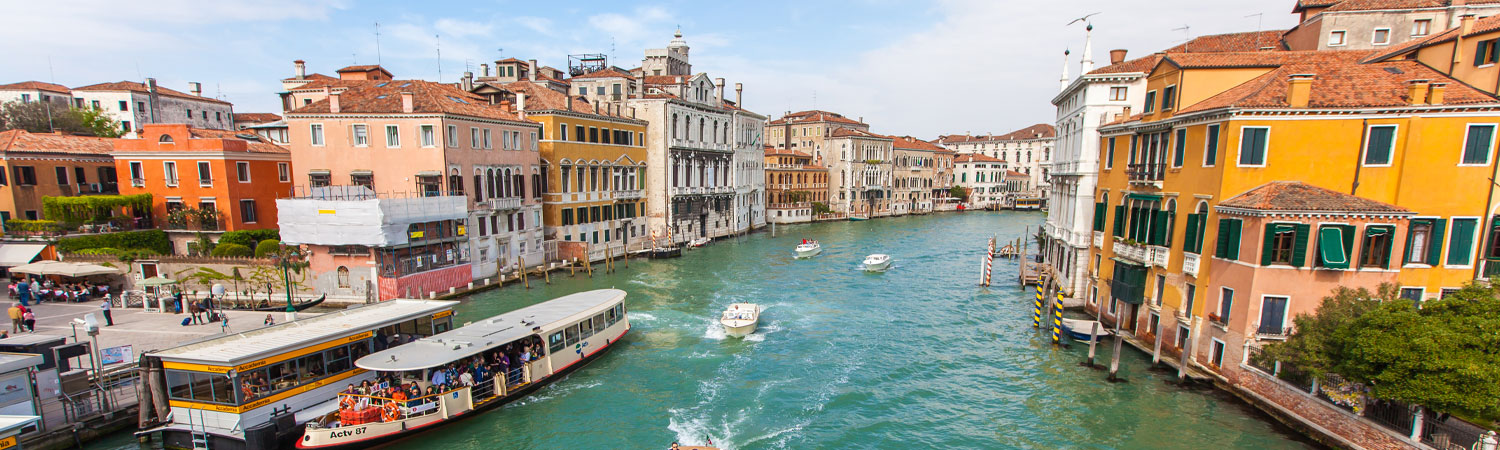 Scenic view of Venice with colorful buildings lining the Grand Canal, boats navigating the waters, and a crowded public transport boat station.