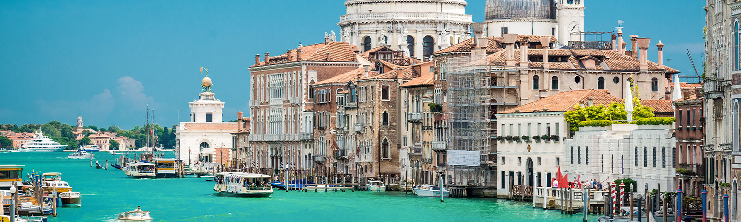 Panoramic view of the Grand Canal in Venice, showcasing historic architecture, boats navigating turquoise waters, and a clear blue sky.