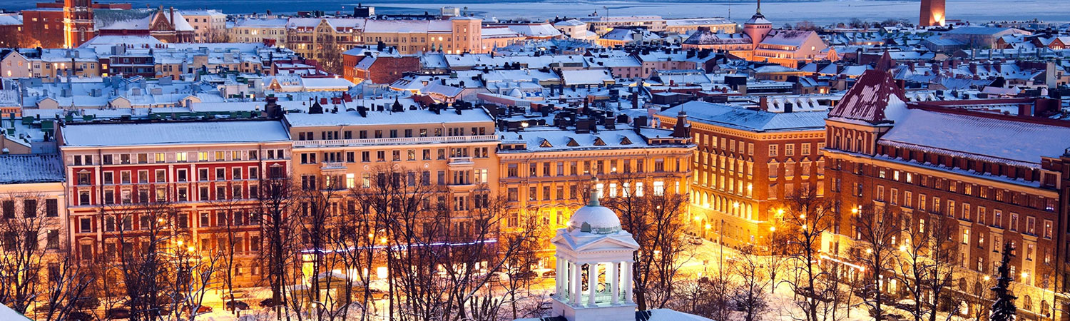 Panoramic view of a snow-covered city at dusk, with illuminated buildings, a gazebo in the foreground, and a serene atmosphere.