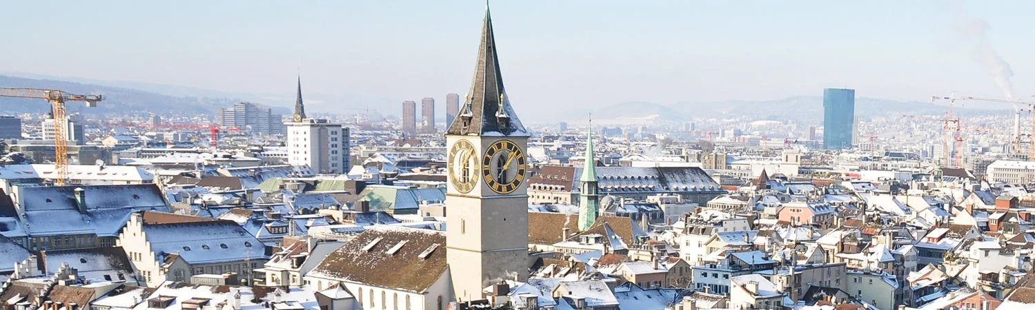 Panoramic view of a cityscape with densely packed buildings, a prominent clock tower, and distant hills under a clear sky