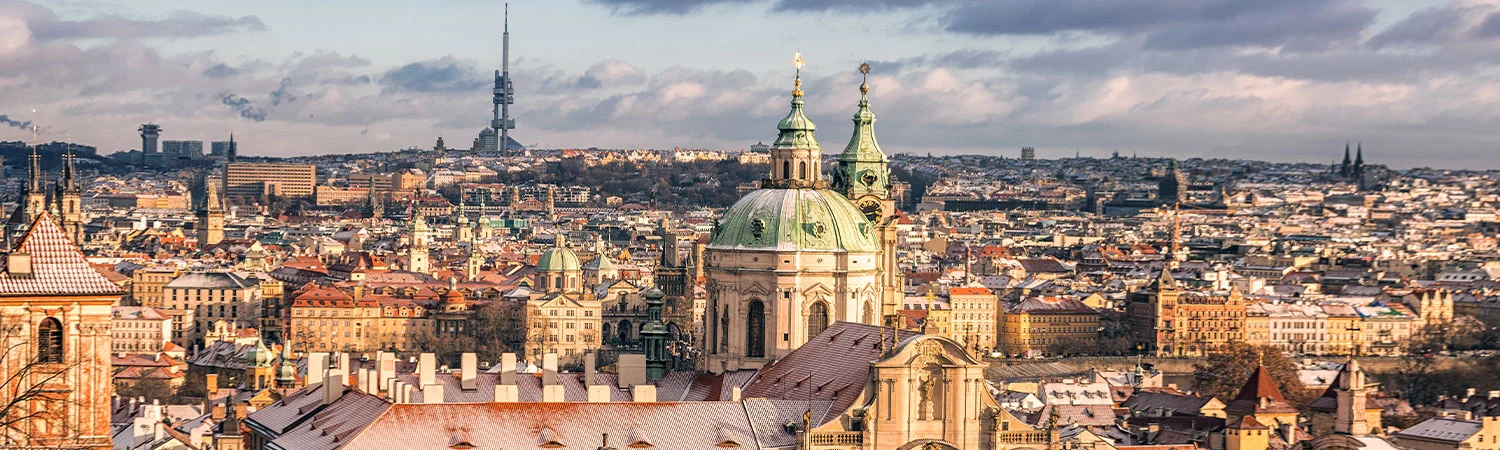 A panoramic view of Prague, showcasing the city’s sprawling landscape under a partly cloudy sky. The historic domed church stands out, symbolizing the city’s rich historical background.