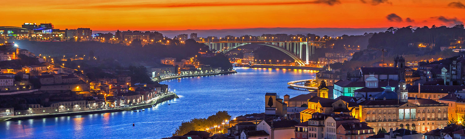 A breathtaking view of a cityscape at dusk in Porto, showcasing the vibrant lights reflecting off the calm waters, with the iconic bridge connecting two parts of the city.