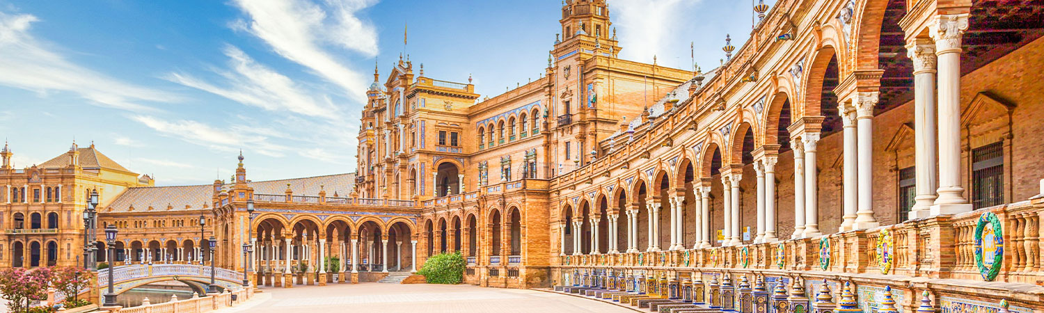 A panoramic view of the vibrant and intricate architecture of Plaza de España in Seville under the bright blue sky.
