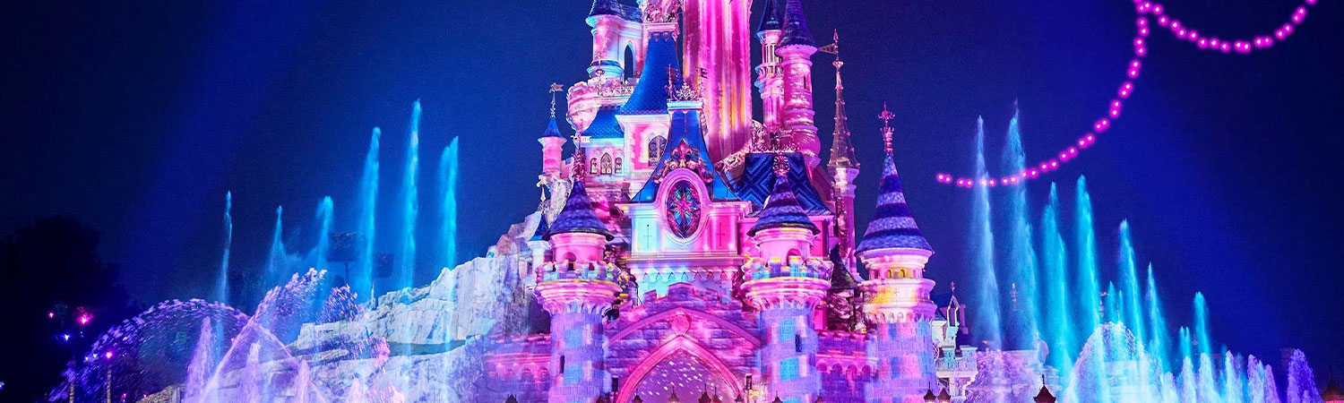 The image captures a breathtaking night view of the iconic Disneyland castle, brilliantly illuminated with multicolored lights that highlight its intricate architectural details.