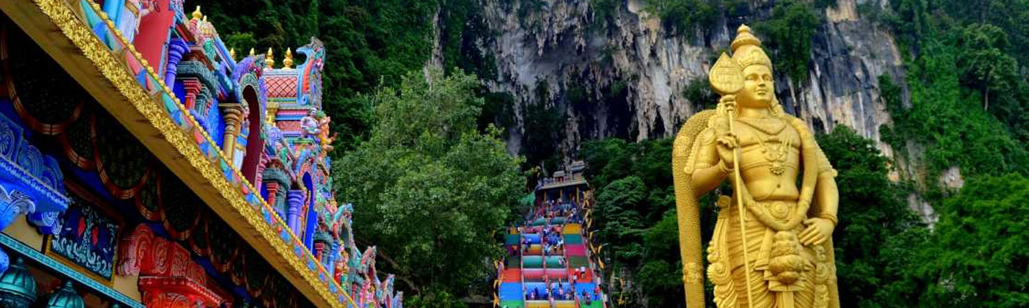 Colorful temple entrance with intricate designs, leading to a staircase that ascends towards a cave in the mountain, flanked by a large golden statue.”  The location of this image is Batu Caves, a famous Hindu temple complex in Kuala Lumpur, Malaysia