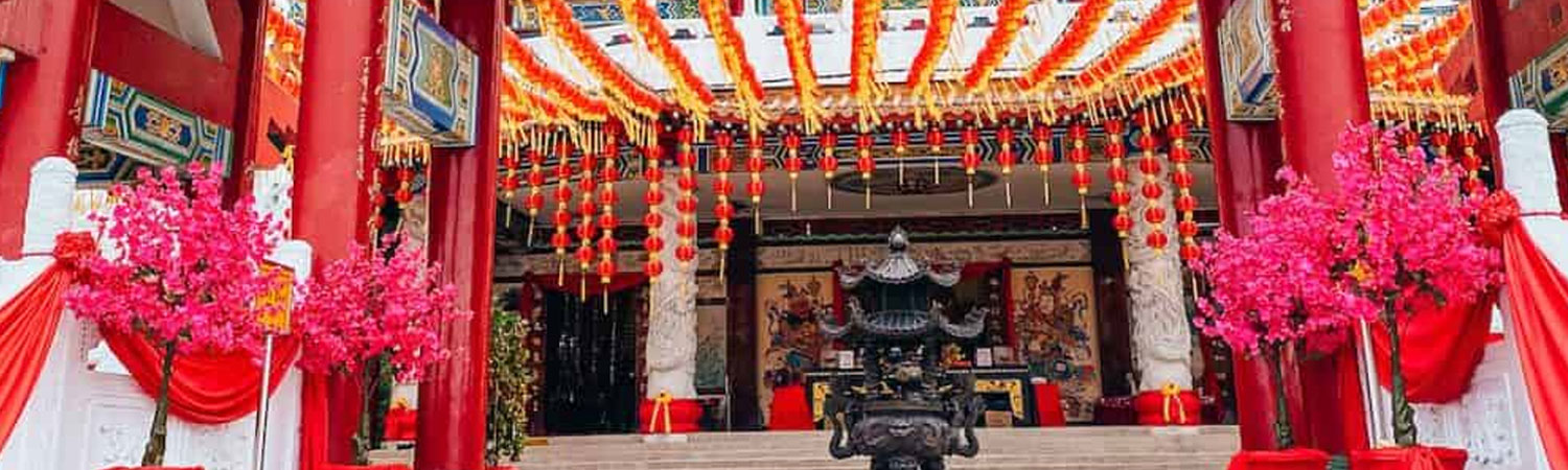 Colorful temple entrance with red lanterns, festive decorations, and pink flowers.