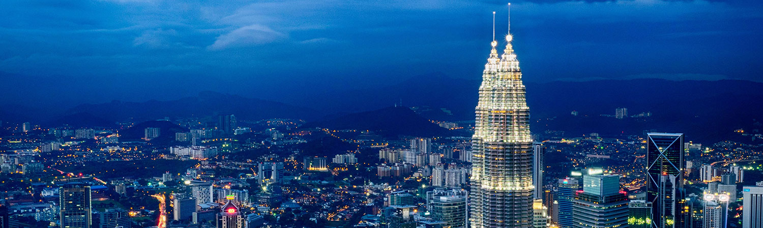 Panoramic view of Kuala Lumpur at dusk with Petronas Twin Towers and cityscape.