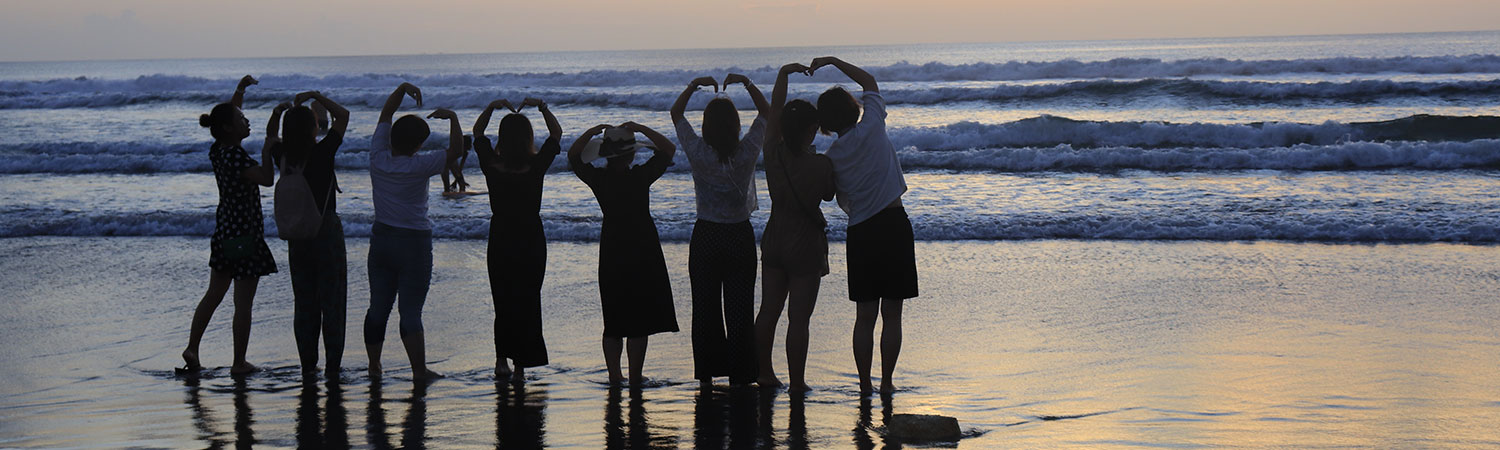 People forming heart shapes at sunset beach with silhouettes and waves.