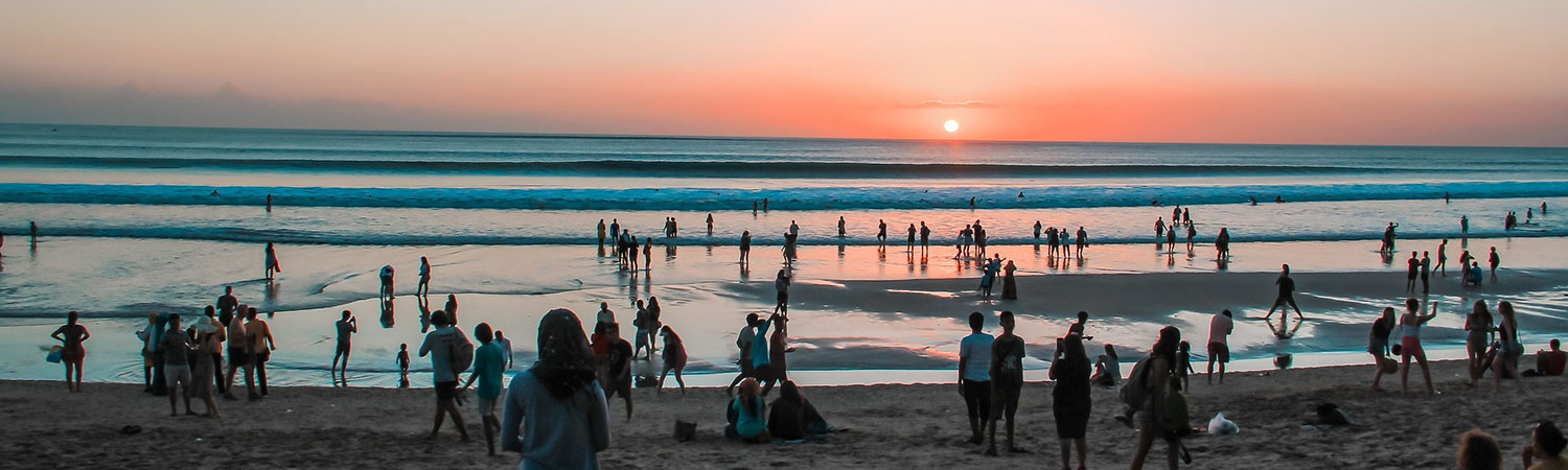 People enjoying sunset on Kuta Beach Bali with calm waves and silhouettes.
