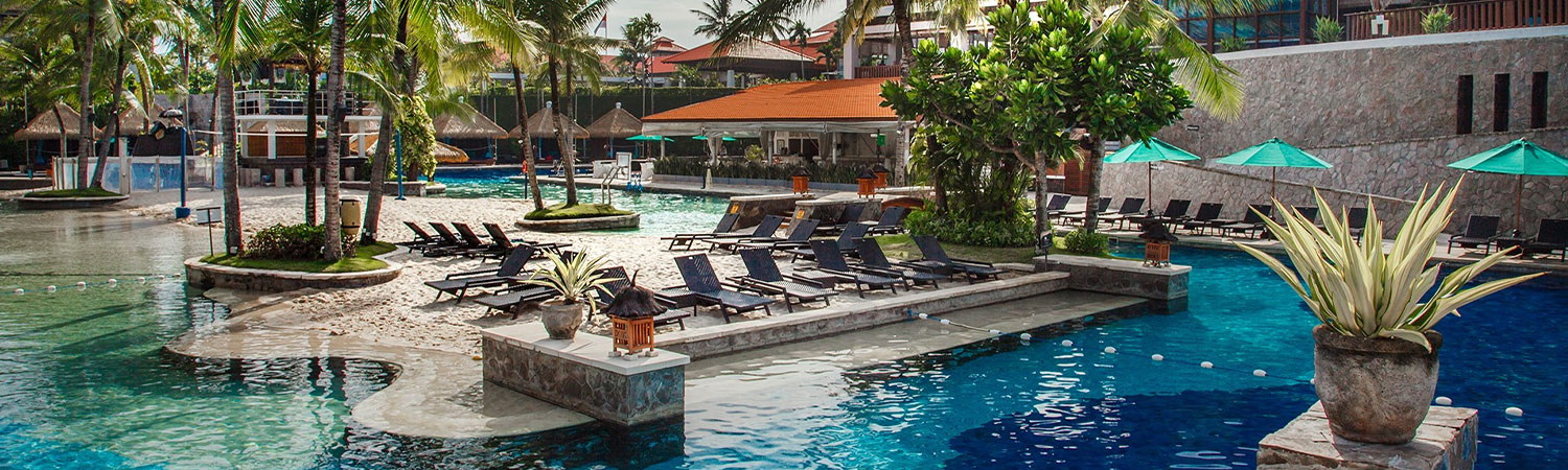 Luxurious resort pool at the Hard Rock Hotel in Bali, surrounded by palm trees, lounge chairs, and umbrellas, offering a serene and tropical ambiance for relaxation.