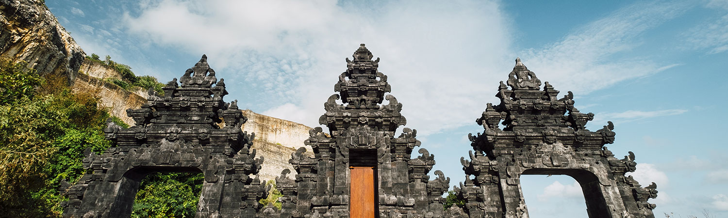 Ancient stone temple gates at a historic site in Bali, surrounded by natural beauty under a clear blue sky.