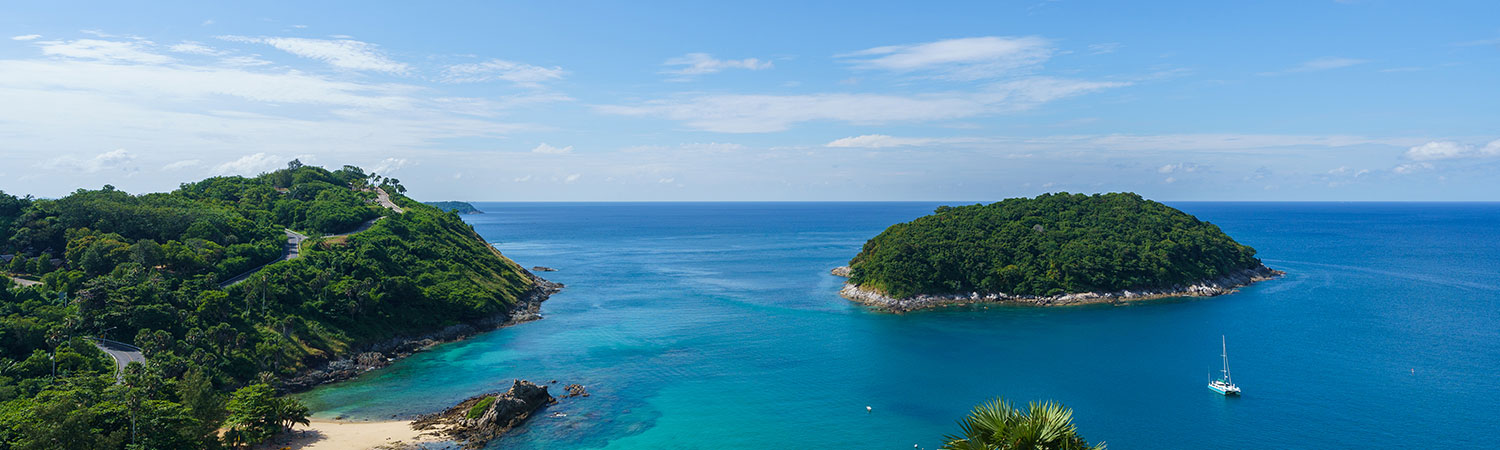 Panoramic view of a tropical coastline with lush greenery, a pristine beach, turquoise waters, and an island, under a clear blue sky.