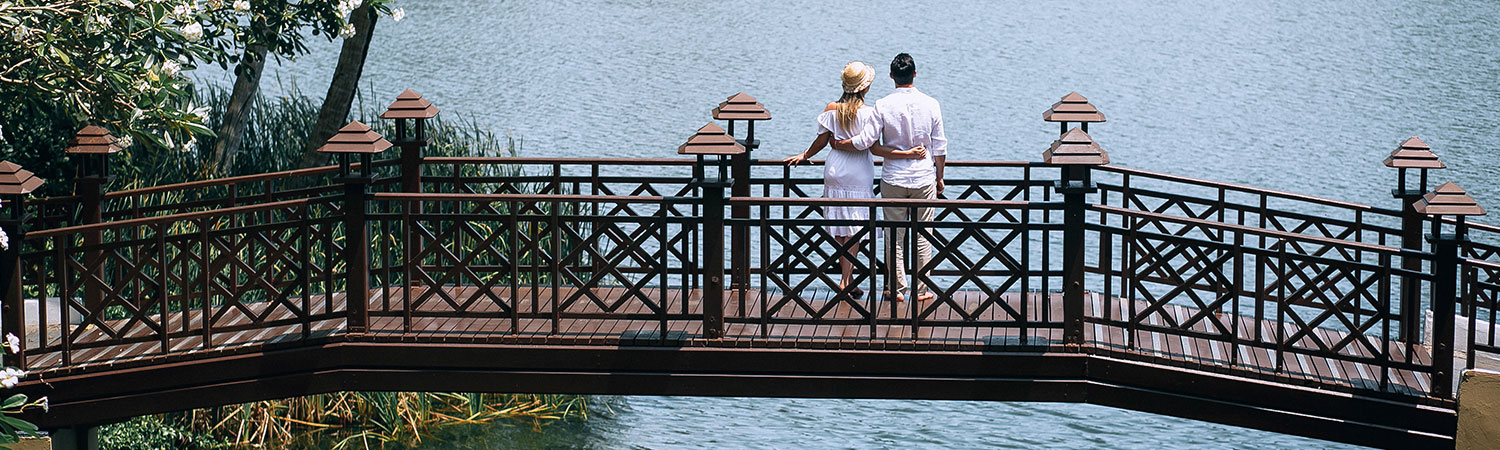 Two people enjoying a tranquil moment on a scenic wooden bridge overlooking a serene lake, surrounded by lush greenery