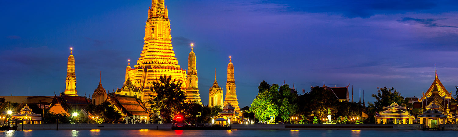 Twilight view of the illuminated Wat Arun temple reflecting on the Chao Phraya River in Bangkok, Thailand.