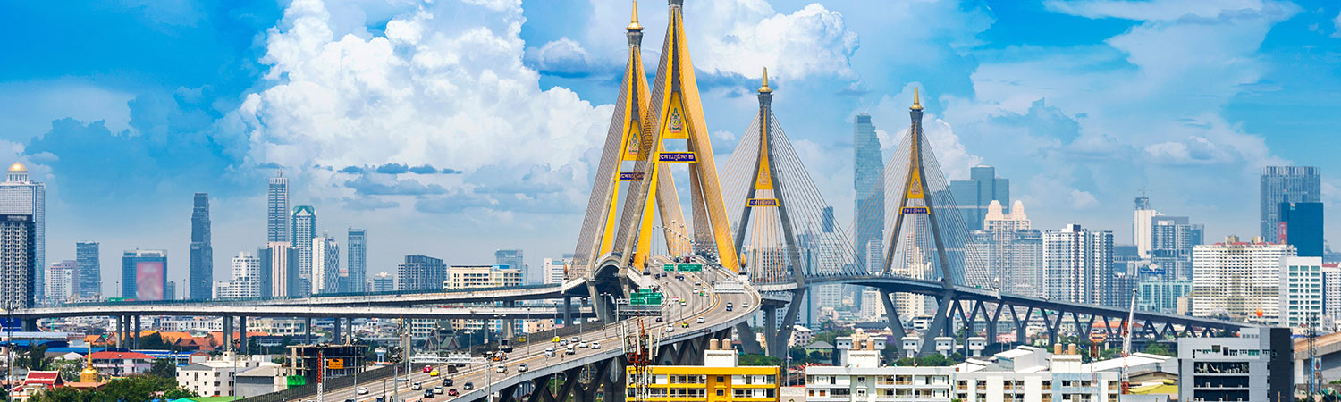 Panoramic view of the Bhumibol Bridge, also known as the Industrial Ring Road Bridge, with Bangkok cityscape and skyscrapers under a blue sky.
