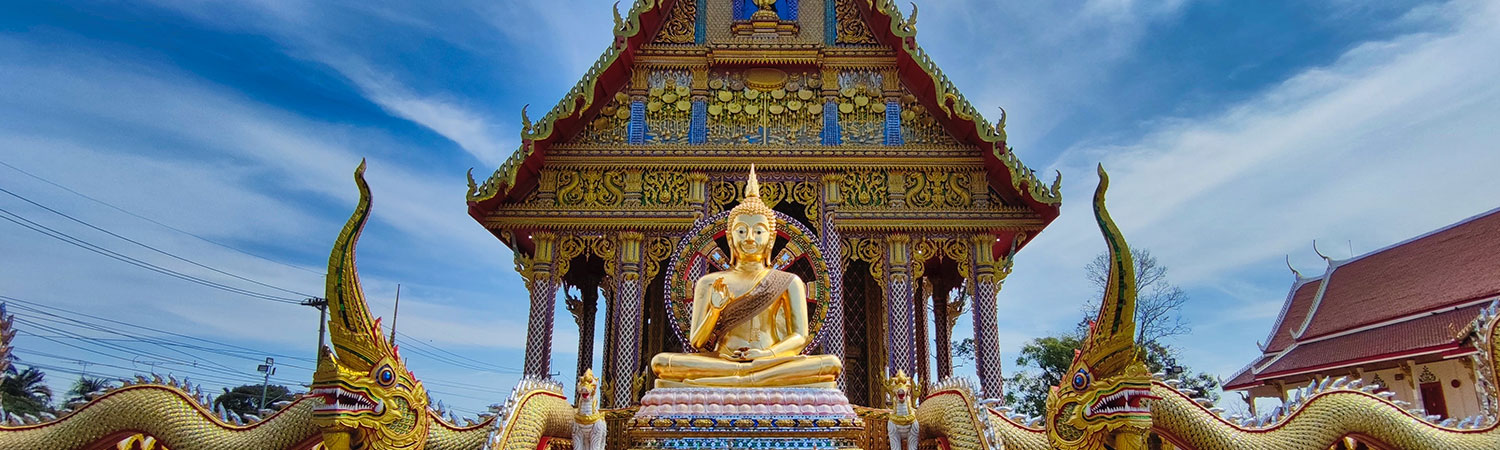 A golden Buddha statue seated in a meditation pose, surrounded by intricate architectural details of a temple, with dragon sculptures on the sides under a clear blue sky.