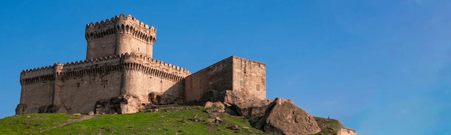 An ancient castle on a rocky hill in Azerbaijan, with green grass and blue sky.