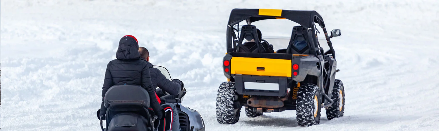 A person riding a snowmobile and a yellow utility task vehicle (UTV) on a snowy terrain in Georgia, showcasing outdoor winter activities.