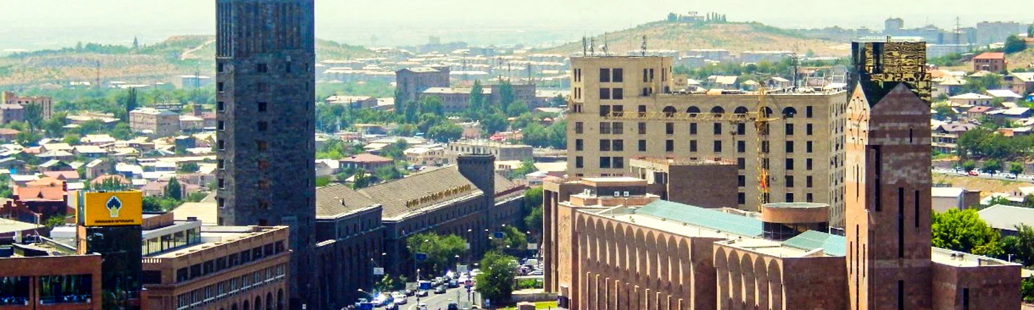 A panoramic view of Yerevan cityscape, showcasing architectural diversity, modern and historical buildings, with a clear sky and distant mountains.