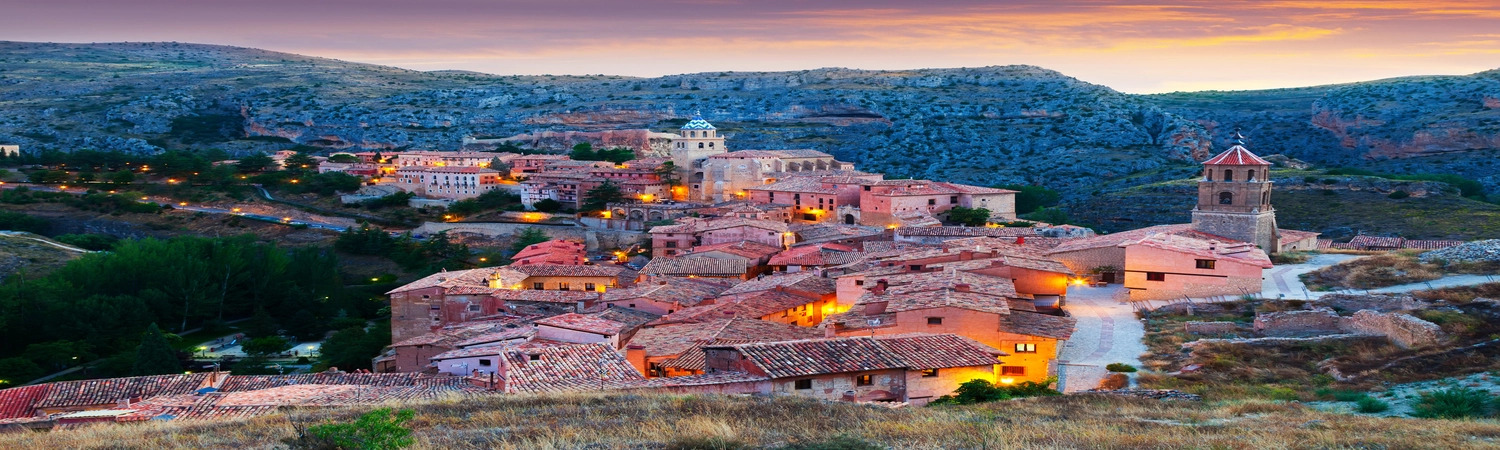  A picturesque view of a historic village nestled among rugged hills, illuminated by the warm glow of sunset, showcasing a blend of nature and architecture.