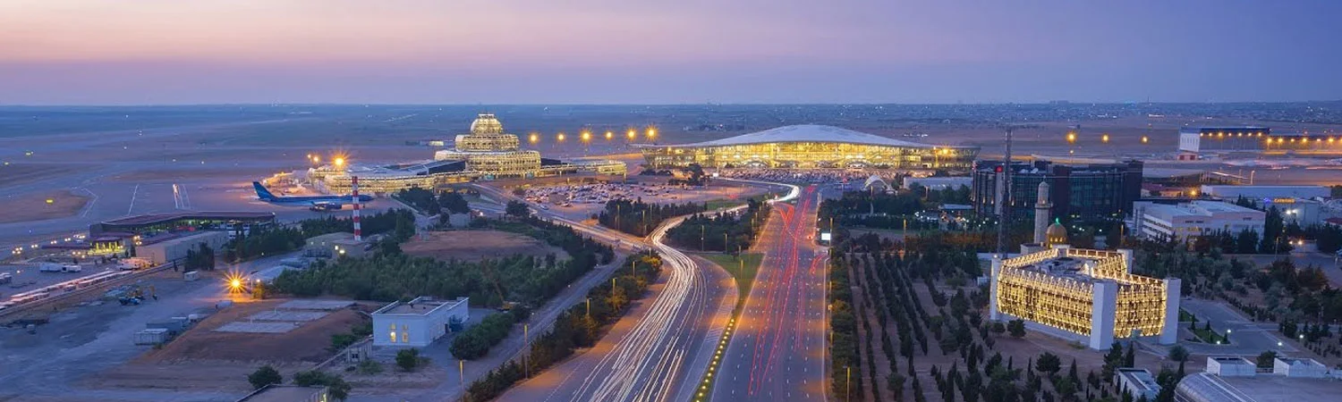 Aerial view of a modern airport terminal at dusk, with a busy highway and adjacent buildings