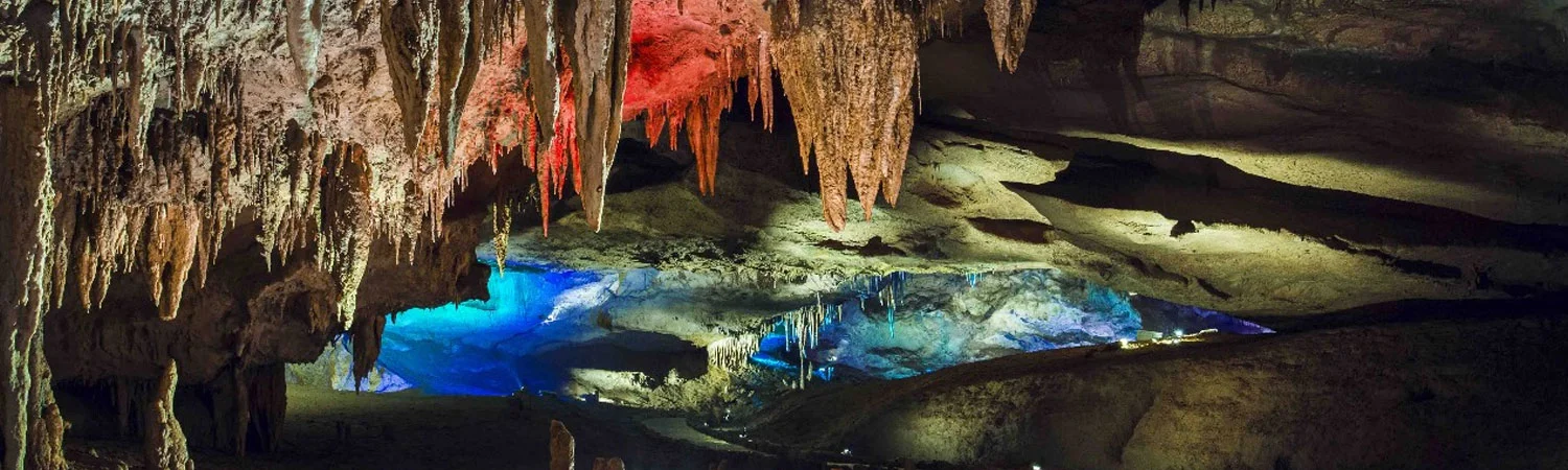 A cave with various stalactites and stalagmites illuminated in red and blue, showcasing geological wonders and natural beauty.