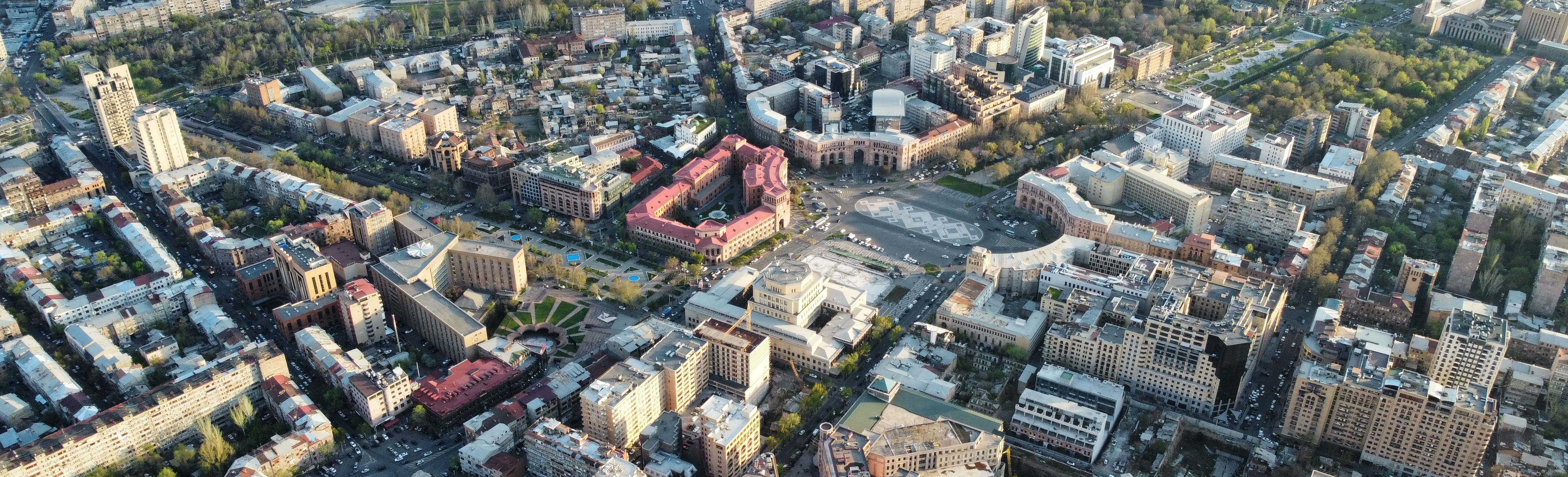 A bird's eye view of Yerevan, Armenia, showing a mix of modern high-rise buildings and historic, golden-colored buildings with red tiled roofs.